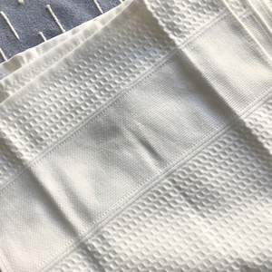May include: A stack of white waffle weave kitchen towels. The towels are folded and have a textured surface.