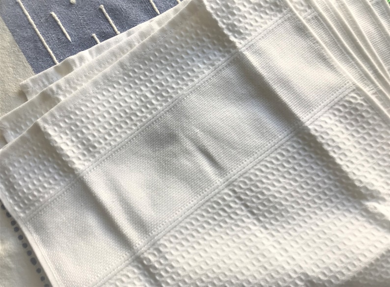 May include: A stack of white waffle weave kitchen towels. The towels are folded and have a textured surface.