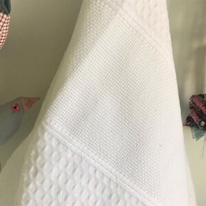 May include: White waffle weave kitchen towel hanging on a hook. The towel is folded in half and has a smooth white section at the top.