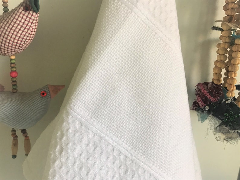 May include: White waffle weave kitchen towel hanging on a hook. The towel is folded in half and has a smooth white section at the top.