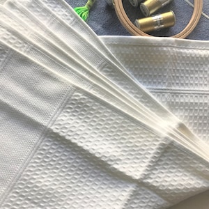 May include: A stack of white cotton dish towels with a waffle weave pattern. The towels are folded in a fan shape.