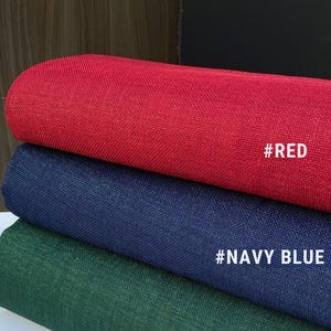 May include: Three fabric swatches in red, navy blue, and green. Each swatch has a textured appearance and is labeled with a hashtag and color name: #RED, #NAVY BLUE, and #GREEN. The fabrics are stacked, showcasing their different hues.