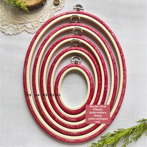 Peut inclure: Ensemble de cinq cerceaux à broder ovales de différentes tailles. Les cerceaux sont rouge antique avec un anneau intérieur crème. Chaque cerceau a un fermoir argenté. Le texte de l'image indique "Nurge Oval Plastic Embroidery Hoop color: antique red."