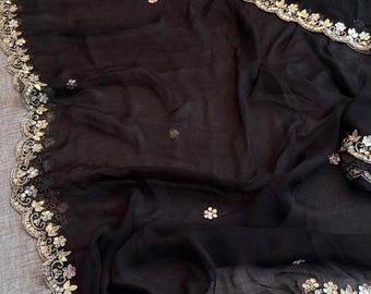 May include: Black sheer fabric with a decorative border. The border features a floral design with silver and gold accents. The fabric is draped, showing its texture and the intricate details of the embellishments.