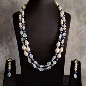 May include: A two-strand necklace with white and blue beads. The necklace is displayed on a black velvet stand. Matching earrings are also included.