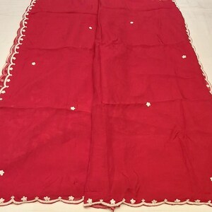 May include: A vibrant red textile with a delicate white scalloped edge. The fabric is adorned with small, evenly spaced white floral accents. The overall design suggests a decorative cloth or garment.