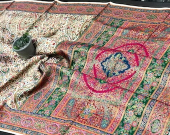 May include: A richly patterned textile with a cream base and detailed floral designs. The fabric displays a vibrant colour scheme with red, green, and blue elements. A small potted plant is placed on the fabric, enhancing the visual appeal.
