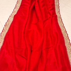 May include: A red saree with a gold embroidered border. The border has a scalloped edge and features intricate floral designs.