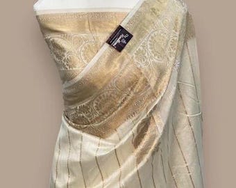 May include: A white and gold saree with a striped pattern and floral embroidery. The saree is draped over a dress form.