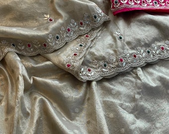 May include: A gold and silver saree with intricate embroidery and embellishments. The saree has a scalloped border with pearl beads and colorful stones. A pink blouse is included.