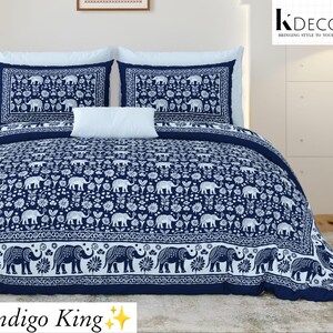 Op de afbeelding: Een kingsize bedset met een donkerblauw en wit patroon van olifanten en bloemmotieven. De set bevat een groot dekbed, twee bijpassende kussenslopen en een klein wit rechthoekig sierkussen. Tekst leest K DECOR en Indigo King.