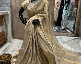 May include: A gold and beige saree with floral embroidery and a pearl necklace. The saree is draped on a mannequin in a store.