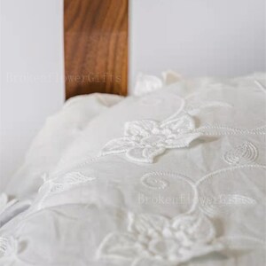 May include: White pillowcase with delicate floral embroidery. The embroidery features a repeating pattern of white flowers and vines.