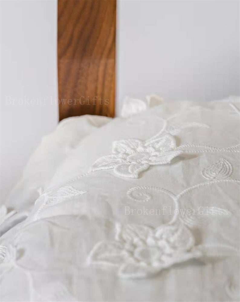 May include: White pillowcase with delicate floral embroidery. The embroidery features a repeating pattern of white flowers and vines.