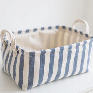 May include: A rectangular storage basket with blue and white vertical stripes. The basket has two white handles and a white interior. The text "Brokenflower Gifts" is printed on the side of the basket.