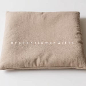 May include: A light brown square cushion with a smooth, textured surface. The cushion is made of a soft, natural fabric.