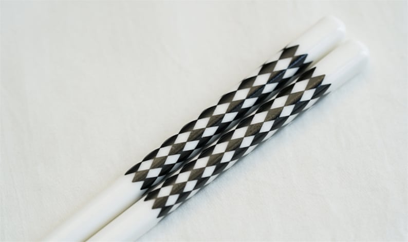 May include: A pair of white chopsticks with black and white diamond patterned accents.