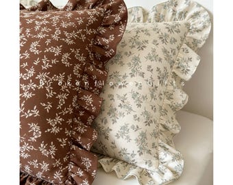 May include: Two decorative throw pillows with floral patterns. One pillow is brown with white floral sprigs, the other is off-white with blue-green floral sprigs. Both pillows have ruffled edges and the text "Broken Flower Gifts".