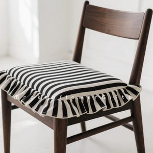 Puede incluir: Silla de madera oscura con cojín con rayas horizontales blancas y negras y borde con volantes. El texto "Broken flower Gifts" es visible en el cojín. El conjunto está sobre un fondo claro.