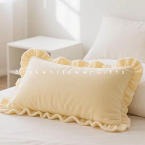 May include: A rectangular, pale yellow pillow with a ruffled edge, resting on a white bed. The pillow has a soft, plush appearance. The text "Brokenflower Gifts" is visible on the pillow.