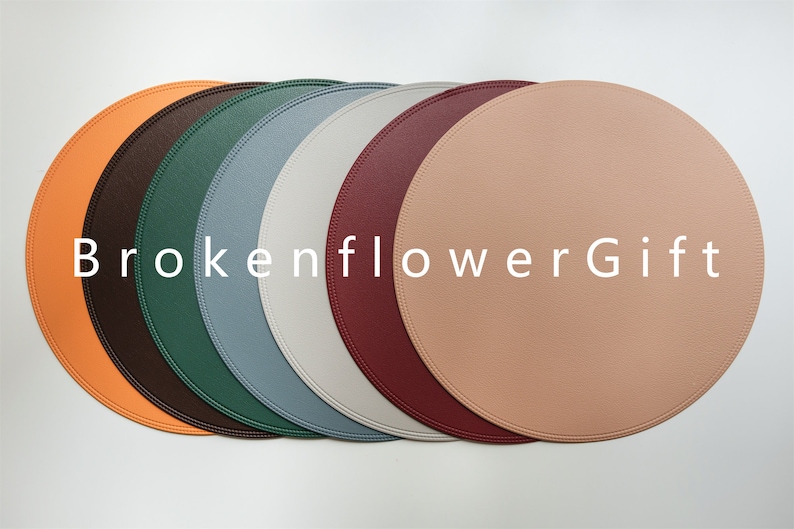 May include: Set of six round leather placemats in various colors, including orange, brown, green, blue, gray, and pink. The placemats are arranged in a row and have a stitched edge.