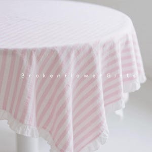 Peut inclure: Une nappe ronde à rayures verticales roses et blanches. La nappe a un bord festonné blanc. Le texte "Brokenflower Gifts" est imprimé sur la nappe.