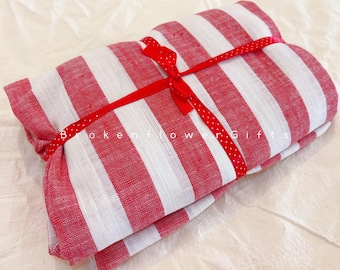 May include: A folded textile featuring a pattern of vertical red and white stripes. The fabric is secured with a thin red ribbon decorated with small white polka dots, tied in a bow. The text BrokenflowerGifts is visible on the fabric.