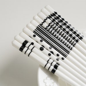 May include: Set of white chopsticks with black geometric patterns. The patterns include polka dots, stripes, zigzags, and checkerboard.