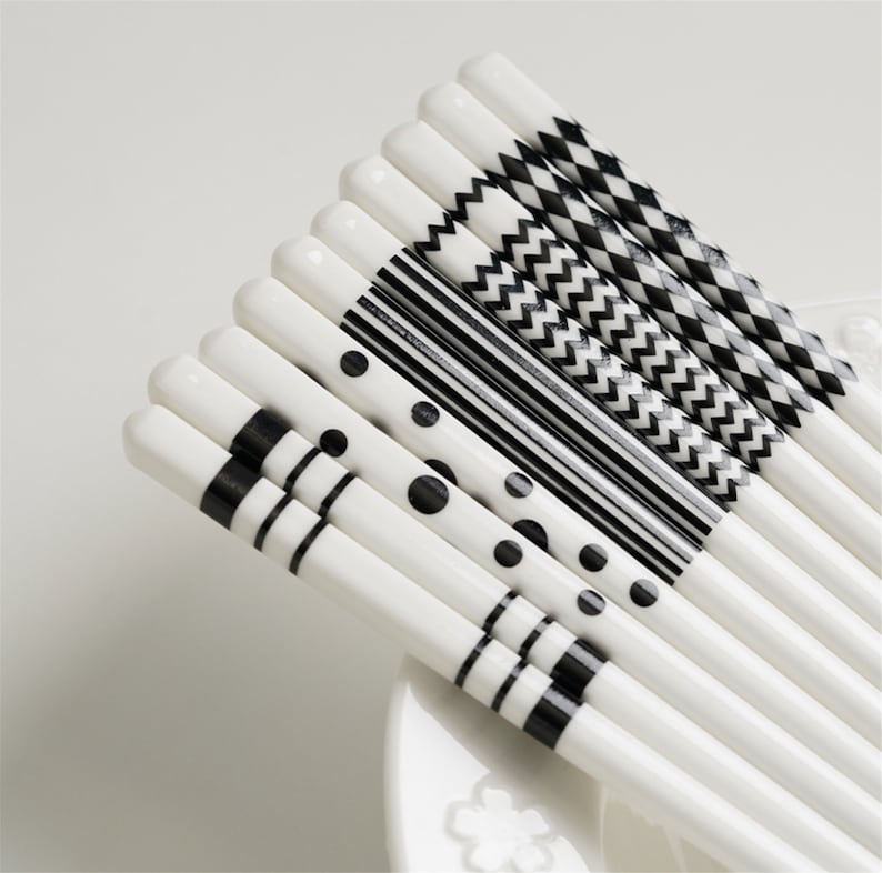 May include: Set of white chopsticks with black geometric patterns. The patterns include polka dots, stripes, zigzags, and checkerboard.