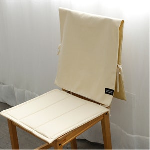 May include: A cream-colored chair cushion with a matching back cushion. The cushion has a quilted design and the back cushion has a label that reads "It's Easy to Decorate".