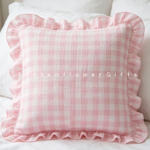 May include: A square throw pillow featuring a light pink and white gingham check pattern with a ruffled border. The text BrokenflowerGifts is printed in white across the center of the pillow, which has a soft, textured fabric appearance.
