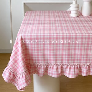 May include: A pink and white gingham tablecloth with a frilled edge. The tablecloth covers a white table. The text "Brokenflower Gifts" is printed on the tablecloth.