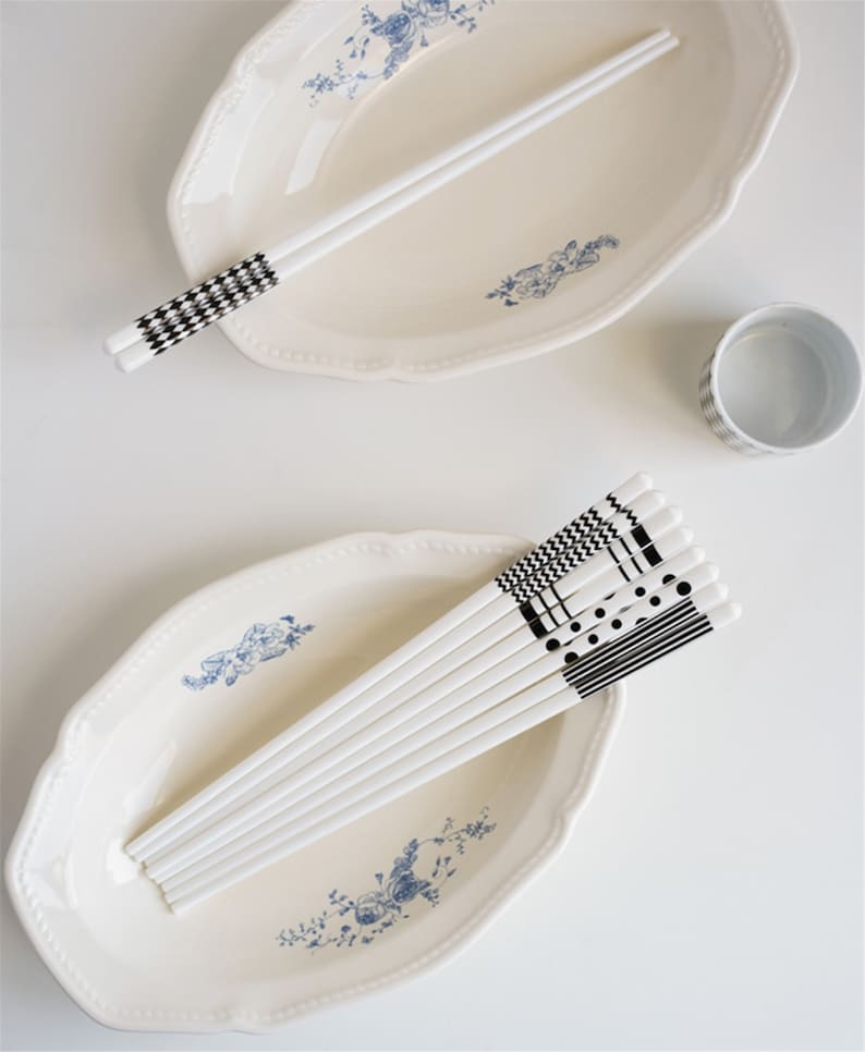 May include: A set of white chopsticks with black and white geometric patterns. The chopsticks are arranged in a bowl and on a plate with a blue and white floral design.