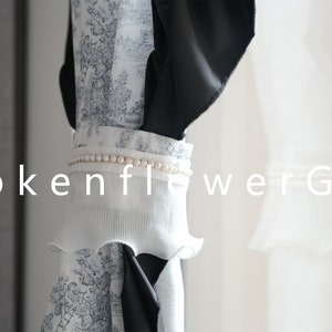 May include: Close-up of a decorative fabric featuring a black and white toile design. The fabric has a white pleated ruffle and a pearl beaded trim. The text "BrokenflowerGift" is displayed in white.