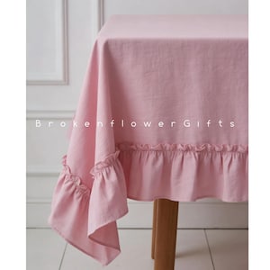 May include: A pale pink linen tablecloth with frilled edges. The tablecloth is draped over a wooden table. The text "Brokenflower Gifts" is visible on the tablecloth.