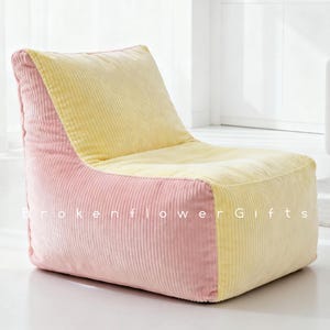 Puede incluir: Un sillón puf de pana en una combinación de colores pastel. La silla presenta una combinación de rosa y amarillo, con el rosa en los laterales y el amarillo en el asiento y el respaldo. El texto "Brokenflower Gifts" es visible en la parte delantera.