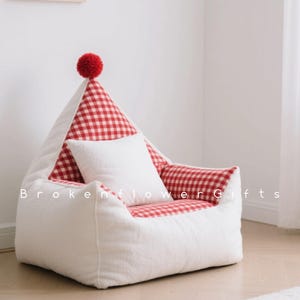 May include: A white beanbag chair with a red and white checked interior and a white cushion. The chair features a red pom-pom at the top. The text "Broken Flower Gifts" is printed on the front of the chair.