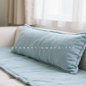 May include: A light blue corduroy rectangular cushion and matching seat cover on a white sofa. The cushion has a stitched border and the text "Brokenflower Gifts" is printed on the cushion.