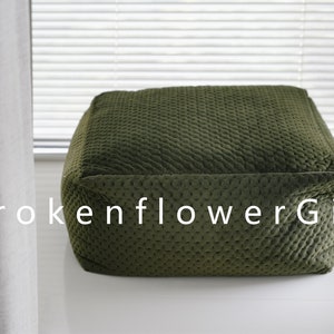 May include: A dark green, square-shaped, quilted floor cushion. The cushion has a textured surface and is made of a soft fabric.