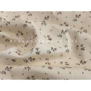 May include: Cream-colored fabric with a delicate floral pattern. Small, dark blue and brown flowers are scattered across the fabric. The text "Brokenflower Gifts" is printed on the fabric.