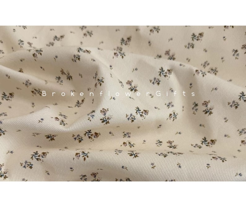 May include: Cream-colored fabric with a delicate floral pattern. Small, dark blue and brown flowers are scattered across the fabric. The text "Brokenflower Gifts" is printed on the fabric.