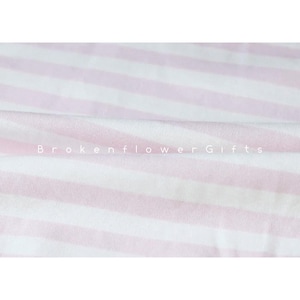 May include: A close-up of a soft, striped fabric in white and light pink. The stripes run horizontally across the frame. The text "Brokenflower Gifts" is printed in white across the fabric.