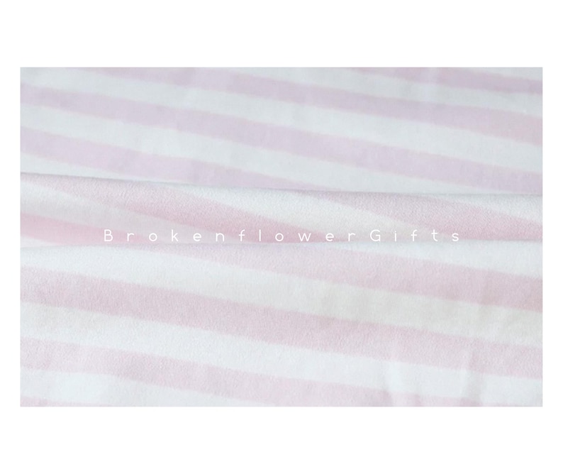 May include: A close-up of a soft, striped fabric in white and light pink. The stripes run horizontally across the frame. The text "Brokenflower Gifts" is printed in white across the fabric.