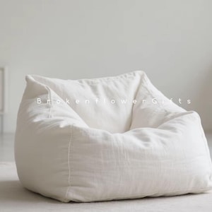 May include: A large, off-white beanbag chair made of soft fabric. The chair is in a relaxed, unstructured shape, with visible seams and folds. The text "Brokenflower Gifts" is printed on the beanbag.