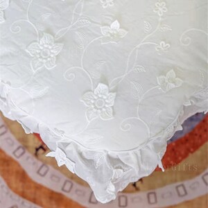 May include: White cotton pillow cover featuring a delicate floral embroidery design. The pillow cover has a ruffled edge and is made from a soft, lightweight fabric.