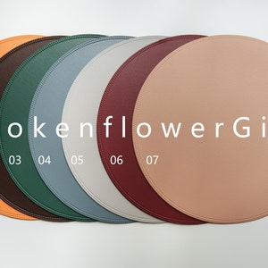May include: Seven round leather placemats in different colors: orange, brown, green, blue, gray, burgundy, and peach. The placemats are arranged in a row with the text "BrokenflowerGift" and numbers 01-07 printed below.