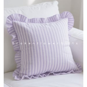 May include: A square cushion featuring vertical lavender and white stripes, edged with a frilled border. The cushion is on a white surface. The text "Brokenflower Gifts" is printed on the cushion.