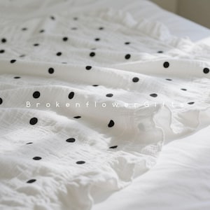 May include: White fabric with black polka dots. The fabric is draped over a surface, with the text "Brokenflower Gifts" visible. The fabric has a ruffled edge.
