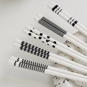 May include: Set of white chopsticks with black geometric patterns. The patterns include stripes, polka dots, zigzags, and checkered designs.