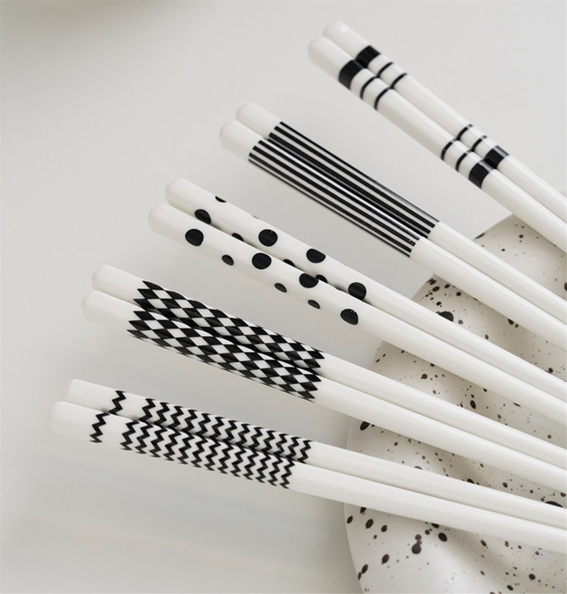 May include: Set of white chopsticks with black geometric patterns. The patterns include stripes, polka dots, zigzags, and checkered designs.